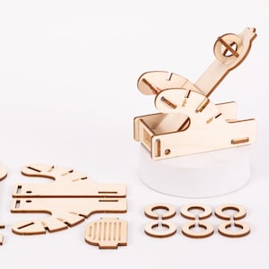 May include: A wooden catapult kit with a base, arm, and a set of wooden rings. The catapult is made of natural wood and is ready to be assembled.