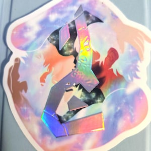 以下が含まれることがあります： 虹色の光沢を持つ、スタイリッシュな数字の6が特徴のホログラフィックステッカー。カラフルな銀河の背景に配置され、白い縁取りとユニークな芸術的デザインが施されています。