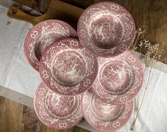 Pode incluir: Um conjunto de seis pratos estampados em vermelho e branco. Cada prato apresenta um design floral e paisagístico detalhado. Os pratos estão dispostos sobre uma superfície de madeira com um pano branco e uma tábua de corte de madeira.