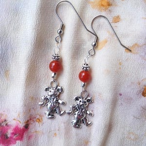 May include: Silver dangle earrings with red carnelian beads and a silver dancing bear charm.