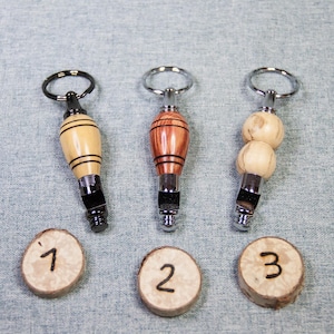 May include: Three wooden keychains with metal rings and whistle attachments. The keychains are made of different types of wood, including light brown, dark brown, and red. The keychains are numbered 1, 2, and 3.