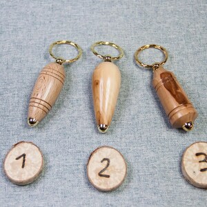 May include: Three wooden keychains with gold rings. Each keychain is a different wood grain pattern and has a gold cap on the end. The keychains are numbered 1, 2, and 3.
