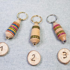 May include: Three wooden keychains with different colored stripes and gold and silver key rings. The keychains are numbered 1, 2, and 3.