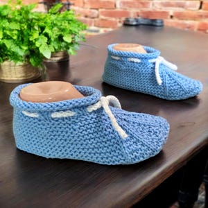 May include: A pair of light blue knitted slippers with white laces. The slippers are on a wooden surface.