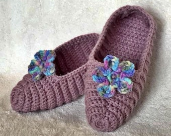 May include: A pair of purple crocheted slippers with colorful flower embellishments. The slippers are soft and cozy, perfect for keeping your feet warm.