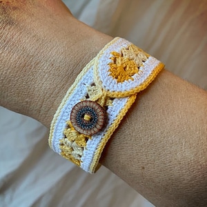 May include: A crocheted bracelet with a yellow and white pattern and a brown button in the centre.
