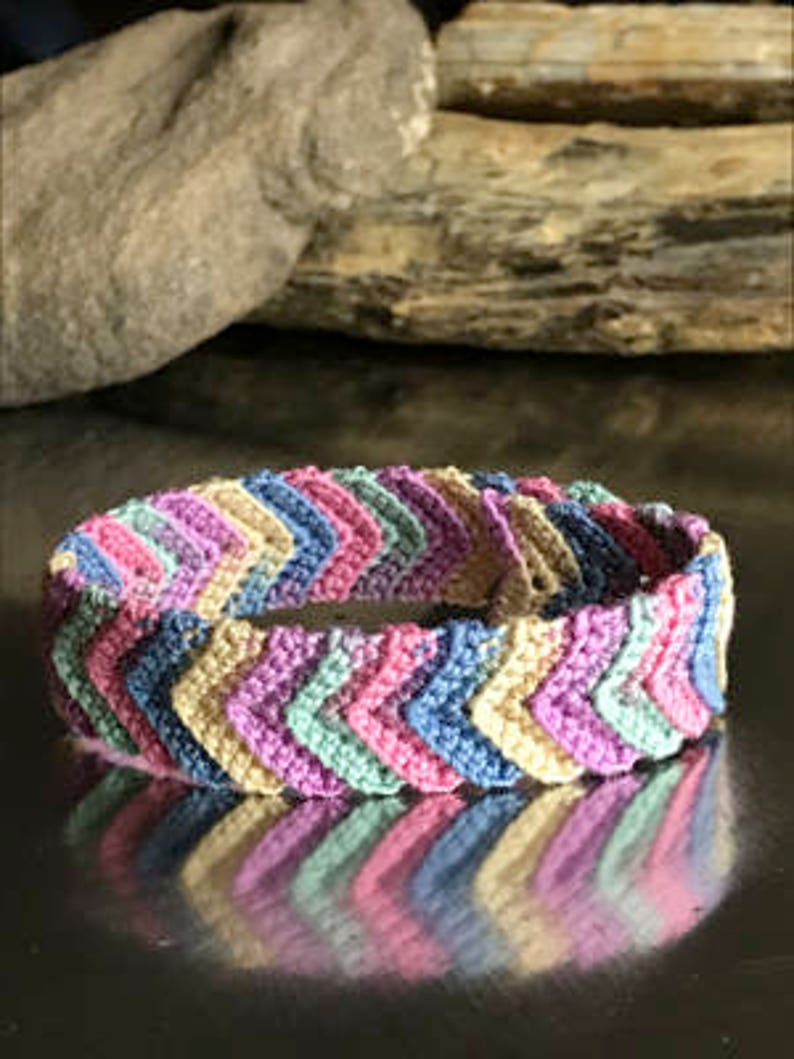 May include: A multi-colored chevron patterned crocheted bracelet with shades of pink, blue, green, and beige.