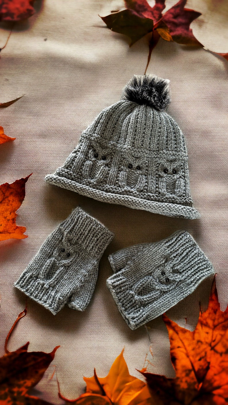 May include: A gray knitted hat with a fluffy pom pom and matching fingerless gloves. The hat and gloves have a cable knit pattern and are decorated with small black buttons. The items are displayed on a beige background with autumn leaves.