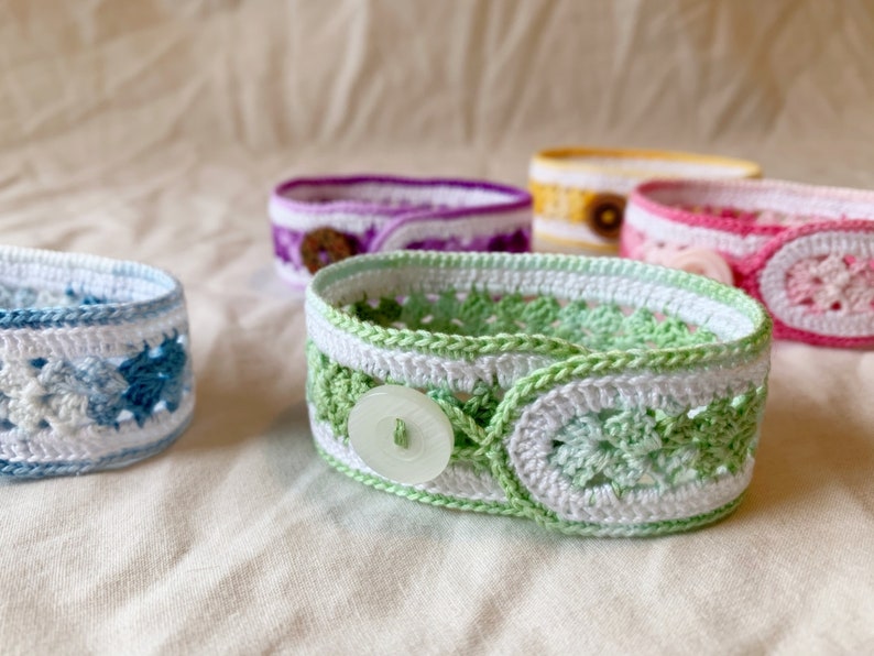 May include: Five crocheted bracelets with different coloured patterns and white buttons. The bracelets are made with a variety of stitches and colours, including blue, green, pink, purple, and yellow.