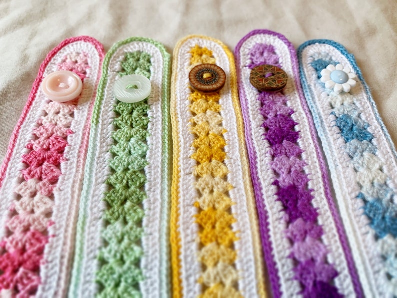 May include: Five crocheted wristlets with different coloured patterns and buttons. The wristlets are pink, green, yellow, purple, and blue.