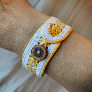 May include: A crocheted bracelet with a yellow and white pattern and a brown button with a blue and white design.