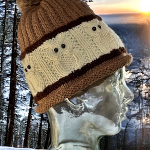 May include: A brown and white knit beanie with a fluffy pom pom on top. The beanie has a brown band with black buttons.
