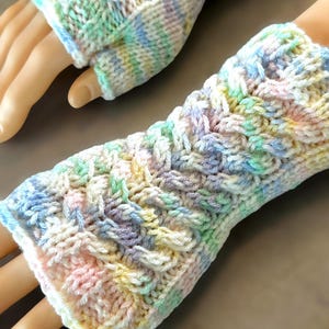 May include: A pair of pastel-colored fingerless gloves with a cable knit pattern. The gloves are made with a soft yarn and have a delicate, feminine look.