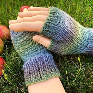 May include: A pair of fingerless gloves in a gradient of green, blue, and purple yarn. The gloves are knitted and have a ribbed cuff.