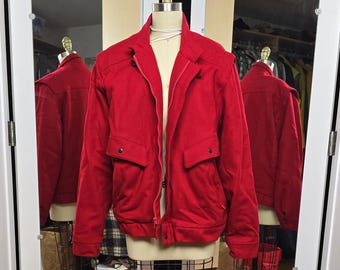 May include: A red bomber jacket with a zip fastening and two large pockets. The jacket is made of a soft, textured fabric.