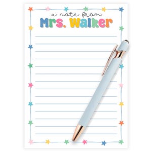 Puede incluir: Un bloc de notas blanco con líneas azules y un borde de estrellas de colores. El bloc de notas tiene el texto "a note from Mrs. Walker" en letras de colores. Un bolígrafo azul claro con punta dorada descansa sobre el bloc de notas.