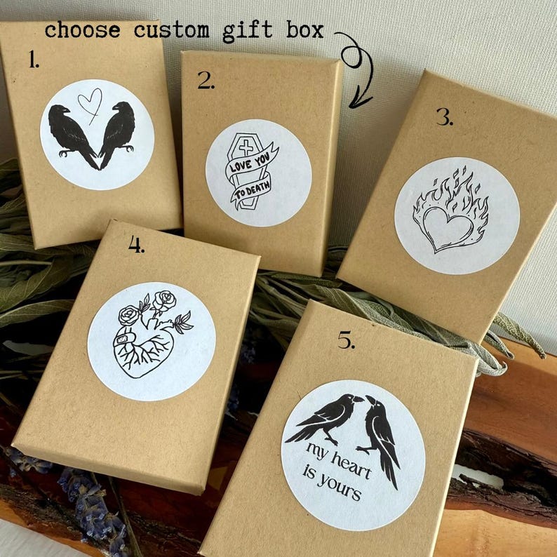 May include: Five small, brown gift boxes with white circular stickers featuring black and white illustrations. The stickers display images of ravens, hearts, roses, and text that reads "LOVE YOU TO DEATH" and "my heart is yours". The text "choose custom gift box" is at the top.