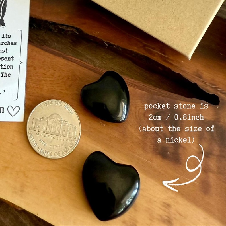May include: Two polished black heart-shaped pocket stones next to a nickel. The text indicates the stones are 0.8 inches in size, about the size of a nickel. The stones are on a wooden surface.