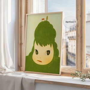 May include: A framed art print featuring a whimsical illustration of a green-haired figure with large eyes and a small house atop its head. The artwork has a light green background and is displayed in a wooden frame.