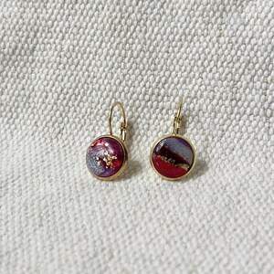 May include: A pair of gold hoop earrings with red and purple resin insets. The resin has a glittery finish.