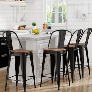 Pode incluir: Quatro bancos de bar de metal preto com assentos de madeira são mostrados em uma cozinha. Os bancos têm um design industrial simples com um encosto curvo. A cozinha apresenta armários brancos e uma bancada de cor clara.