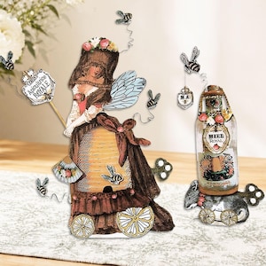 May include: Whimsical decorative items featuring a fairy-like figure, a beehive, and a bottle with the text "MIEL ROYAL". The items are adorned with bees and floral accents, creating a charming, vintage aesthetic. The beehive has a brown and yellow color scheme.
