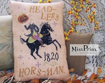 May include: A beige pillow with a cross-stitch design of a headless horseman riding a black horse. The design includes the text "HEADLESS HORSMAN 1820" and a pumpkin with a face. The pillow is on a white lace tablecloth with a branch of yellow flowers.