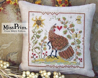 Puede incluir: Un cojín cuadrado blanco roto con un diseño de punto de cruz que representa una gallina marrón con un corazón rojo, rodeada de girasoles, hojas y una mariposa. El texto "Miss Prim. Cross Stitch Pattern" es visible.