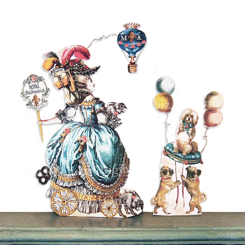 May include: A whimsical paper cutout scene featuring a woman in a blue gown labeled "Royal Balloonist," a hot air balloon, and several dogs. The woman is on wheels, and a small dog is by her side. Other dogs and a poodle are also present.