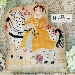 Op de afbeelding: Kruissteekpatroon met een vrouw in een gele jurk die op een wit paard met zwarte vlekken rijdt. De tekst "I do." en "Martha 1959" zijn zichtbaar. Het ontwerp is van Miss Prim.