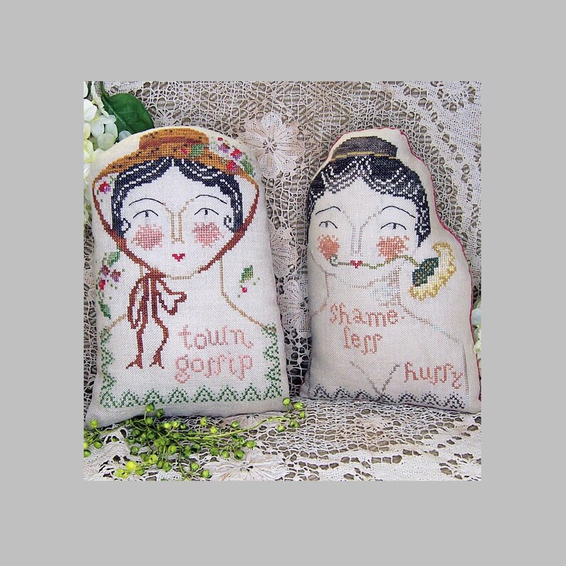May include: Two decorative fabric dolls with embroidered faces and text. One doll wears a hat and says "town gossip." The other doll has a black cap and says "shame less hurry."