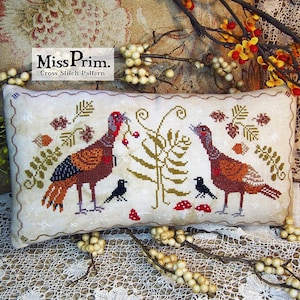 May include: Cross stitch pattern featuring two turkeys, a fern, and four black birds. The turkeys are brown and orange with black and white markings. The fern is green and brown. The birds are black with white beaks. The pattern is on a white background with a brown border.