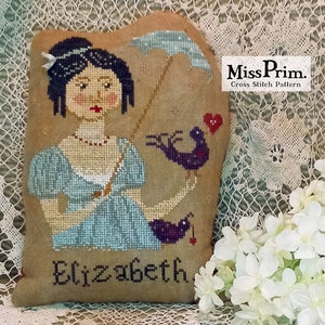 Può includere: Schema a punto croce raffigurante una donna in abito blu con un ombrello e due uccelli viola. Il nome "Elizabeth" è ricamato sotto. Il testo "Miss Prim. Cross Stitch Pattern" si trova in alto a destra.