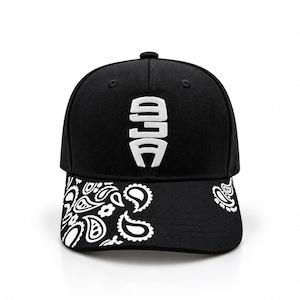 Könnte beinhalten: Eine schwarze Baseballkappe mit einem weißen gestickten Logo auf der Vorderseite. Der gebogene Schirm ist mit einem weißen Paisley-Muster auf schwarzem Grund verziert. Die Kappe hat eine strukturierte Krone und einen Knopf oben.