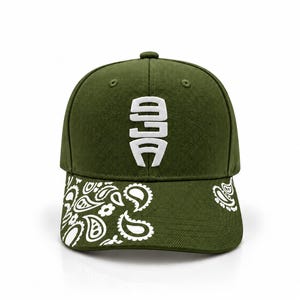 May include: An olive green baseball cap featuring a white embroidered logo on the front panel. The curved brim is decorated with a white paisley pattern that wraps around the sides, contrasting against the solid olive green fabric of the cap.
