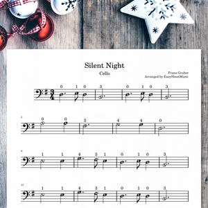 Peut inclure: Partition de musique pour violoncelle de "Silent Night", avec des notes de musique et du texte. La partition est sur une page blanche, avec des décorations de Noël et une décoration en forme d'étoile en arrière-plan.
