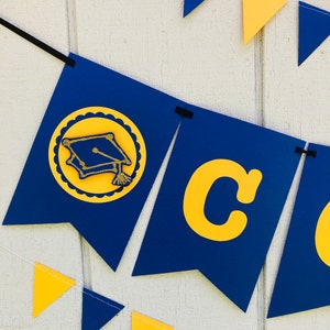 May include: A blue and gold graduation banner with the word "Congrats" and a graduation cap icon. The banner is strung with alternating blue and gold triangle flags.