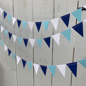 May include: A blue, white, and light blue triangle banner with alternating colors. The banner is strung on a white string and is hanging on a white wooden fence.