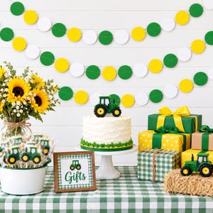 May include: A white frosted cake topped with a green tractor figurine, a bouquet of sunflowers, tractor-shaped cookies in a white bucket, a sign reading Gifts, and wrapped presents on a green and white checkered tablecloth with paper garland.