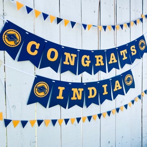 May include: A blue and gold graduation banner with the words "CONGRATS INDIA" and graduation caps on each end.