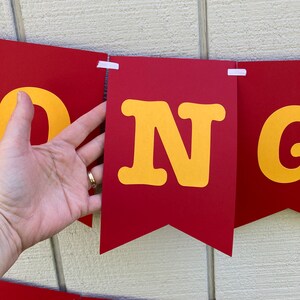 May include: Red and yellow banner with the word "CONGRATS" in large, yellow letters. The banner is made of felt and has a scalloped edge.