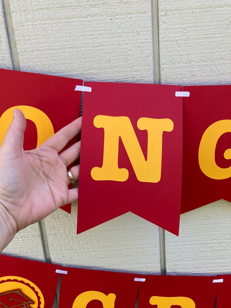 May include: Red and yellow banner with the word "CONGRATS" in large, yellow letters. The banner is made of felt and has a scalloped edge.