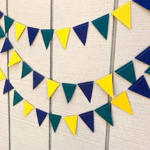 Peut inclure: Une guirlande festive compos&eacute;e de fanions triangulaires jaunes, bleu marine et vert sarcelle. Les fanions sont reli&eacute;s par un fil blanc, cr&eacute;ant une guirlande d&eacute;corative. La guirlande est affich&eacute;e sur un fond en bois blanc.