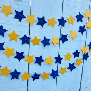 May include: A gold and navy blue star garland with alternating colors. The garland is made of paper stars and is strung together with string.