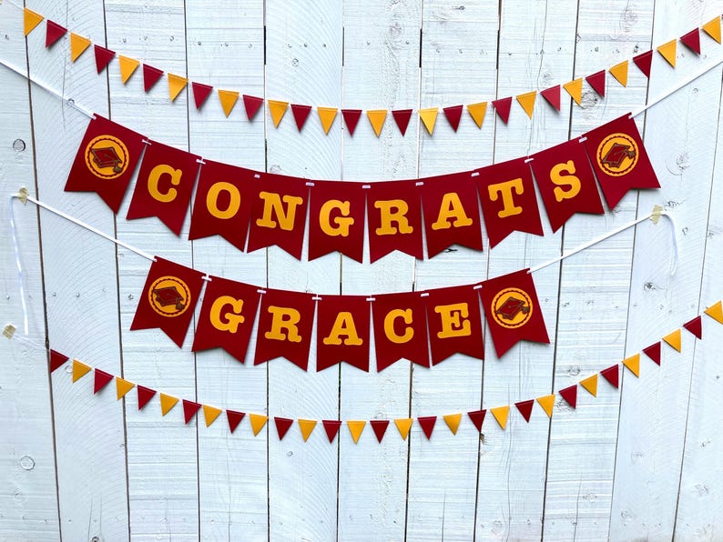 May include: Red and gold graduation banner with the words "Congrats Grace" on it. The banner is strung up on a white wooden fence.