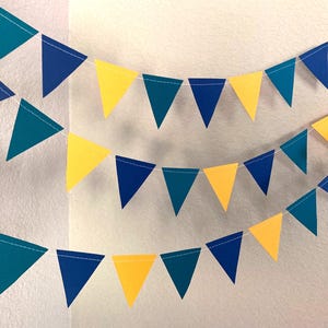 Peut inclure: Trois guirlandes de fanions color&eacute;s dans les tons de turquoise, de bleu et de jaune. Les drapeaux triangulaires sont enfil&eacute;s sur une ficelle blanche, cr&eacute;ant une banni&egrave;re festive. Parfait pour les f&ecirc;tes.