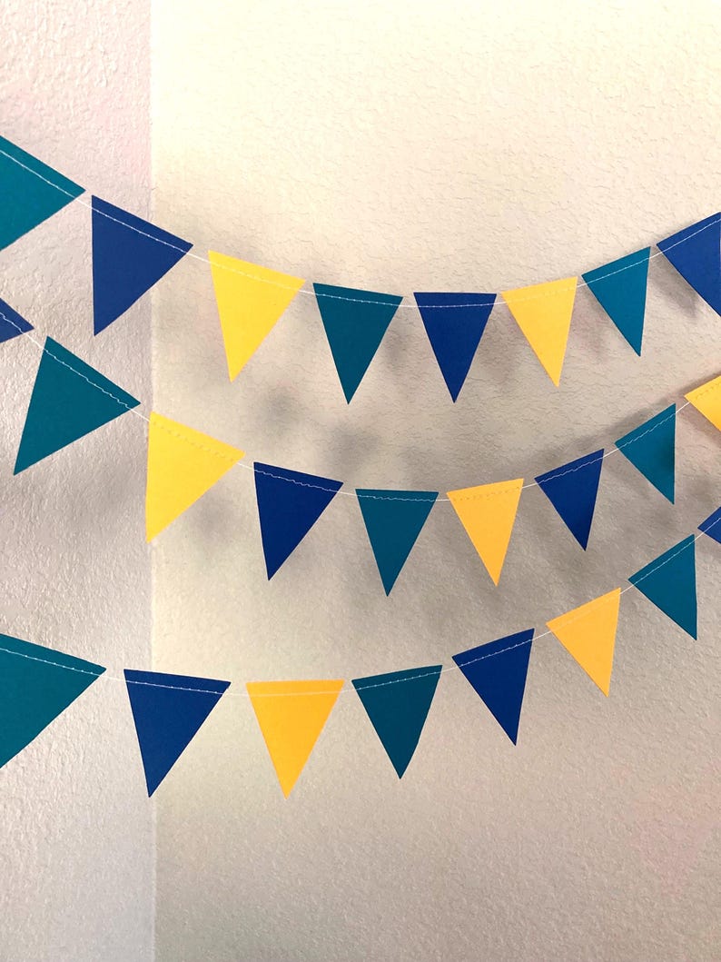 Peut inclure: Trois guirlandes de fanions color&eacute;s dans les tons de turquoise, de bleu et de jaune. Les drapeaux triangulaires sont enfil&eacute;s sur une ficelle blanche, cr&eacute;ant une banni&egrave;re festive. Parfait pour les f&ecirc;tes.