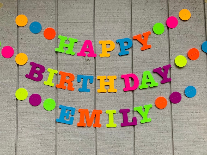 May include: A colorful banner with the words "Happy Birthday Emily" in neon colors. The banner is strung with colorful paper circles.