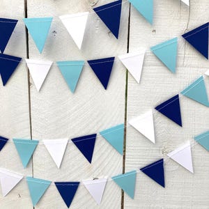 May include: A blue, white, and light blue paper triangle banner. The banner is strung together with white thread. The triangles are evenly spaced and alternate in color.