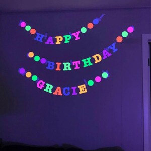 May include: A neon pink, orange, yellow, green, and blue banner with the words "Happy Birthday Gracie" hanging on a wall.